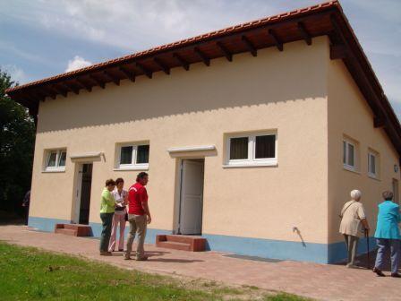 Zwei Gruppen von Personen stehen vor einem neueren, hellen Geb&auml;ude mit mehreren Fenstern und T&uuml;ren.