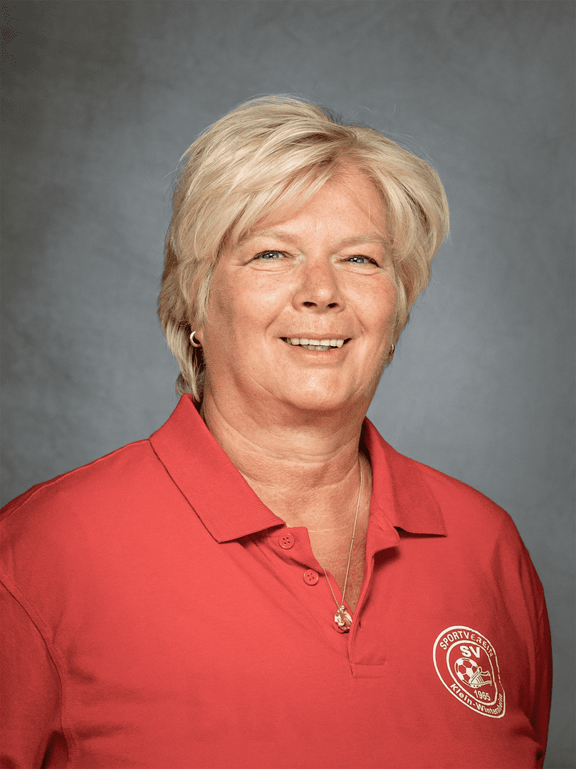 Portr&auml;t einer l&auml;chelnden Frau mit blonden Haaren, die ein rotes Polo-Shirt tr&auml;gt und vor einem grauen Hintergrund steht.