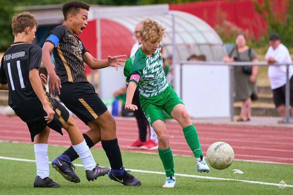 Zwei Jugendliche kämpfen um den Ball auf einem Fußballfeld während eines Spiels. Der Spieler in Grün ist der Kapitän.