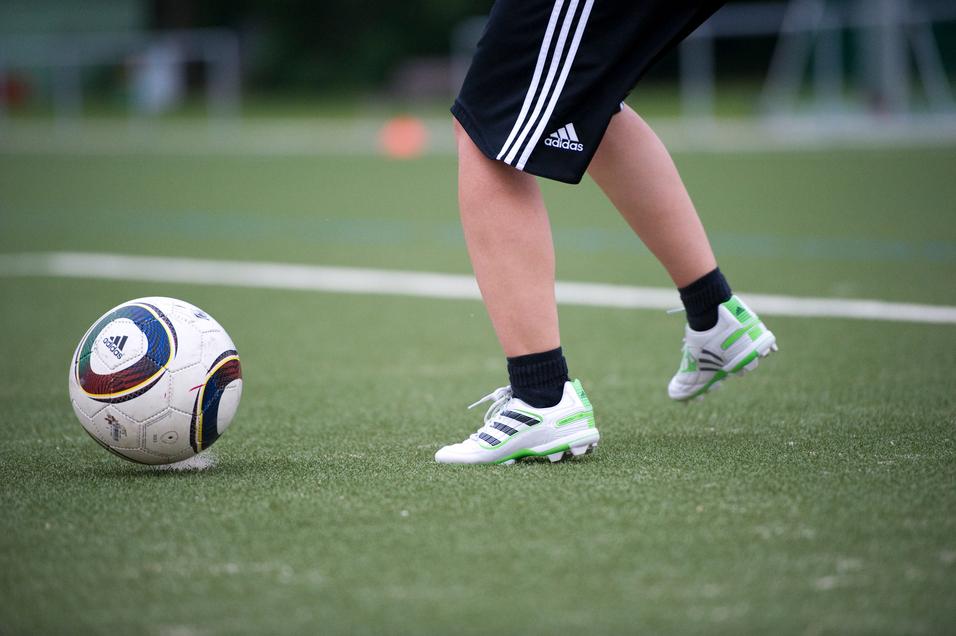 Ein Fuß mit Fußballschuhen tritt auf einen Fußball auf einem Kunstrasenfeld.