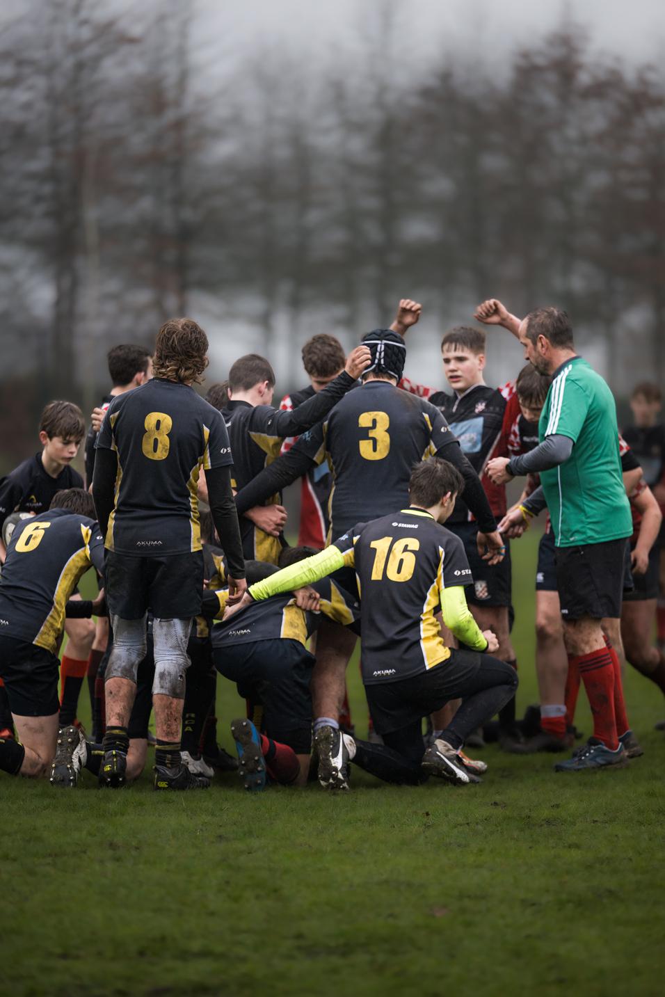 Gruppenspieler auf einem Rugbyfeld umarmen sich, einige tragen die Trikots mit den Nummern 3, 8 und 16.